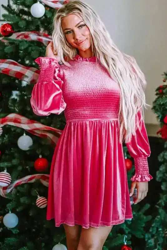 Pink smocked velvet dress with frilled neckline and long sleeves, styled for a feminine and festive look.