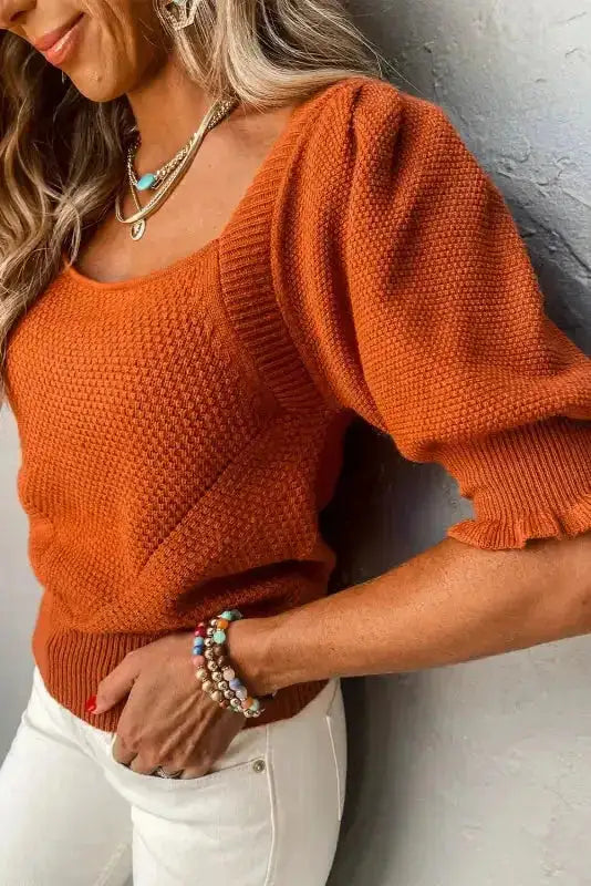 Close-up side view of rust square neck knit top with puff sleeves and textured pattern, styled with layered jewelry.