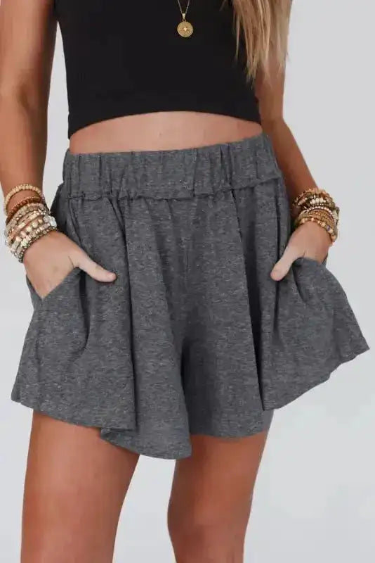 Front view of gray elastic waist Lambada shorts with side pockets, paired with a black crop top for a casual summer outfit.