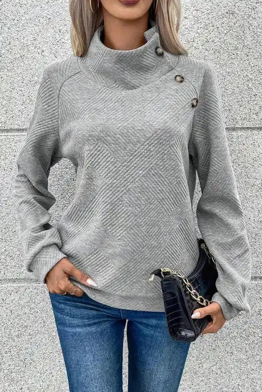 Gray ribbed pullover top with high collar and button details, paired with black clutch for a casual winter style.
