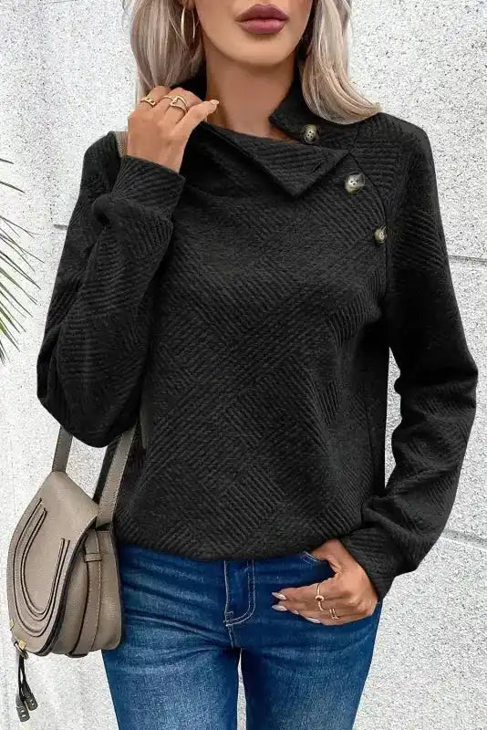 Black ribbed pullover with asymmetrical button collar and long sleeves, styled with a handbag for a chic casual look.