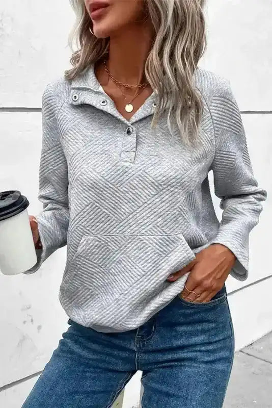 Gray ribbed pullover top with partial button placket and long sleeves, styled casually with jeans and coffee cup.