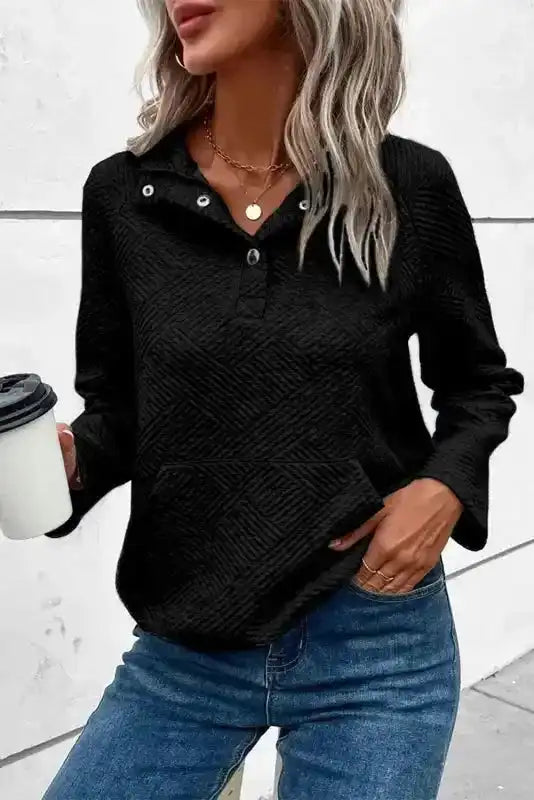 Women's black textured pullover with button collar and long sleeves, styled casually with jeans for a relaxed winter look.