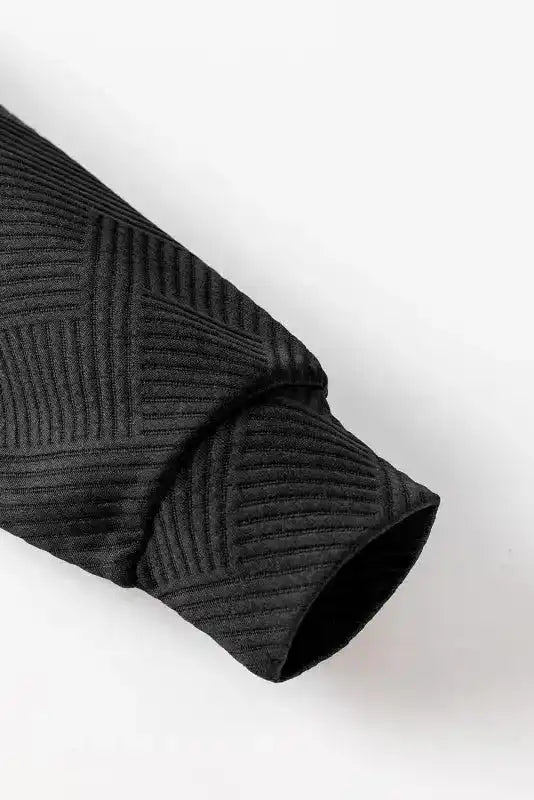 Close-up of black ribbed sleeve showing textured geometric pattern, highlighting fabric detail of winter pullover top.
