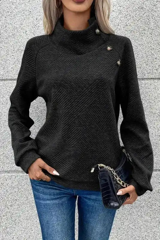 Front view of black ribbed pullover with buttoned high collar and long sleeves, styled with a clutch for a casual winter outfit.