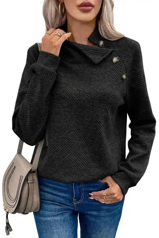 Black textured pullover top with button detail and ribbed pattern, styled with a shoulder bag for a modern casual look.