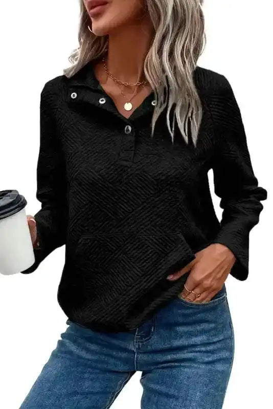 Casual black textured pullover top with button neckline and ribbed fabric, paired with denim for a cozy winter outfit.