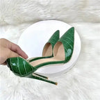 Hand holding croc-effect green stiletto heel to show detailed PU leather texture and pointed toe, perfect for special occasions.