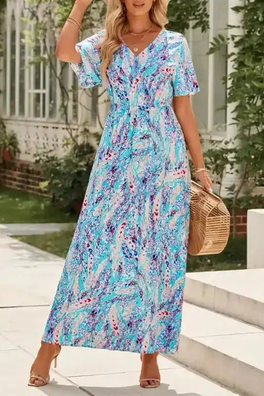 Model wearing green floral wrap maxi dress with V-neck and short sleeves, styled with heels and a bamboo handbag for a chic summer look.