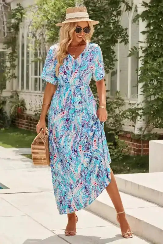 Green floral V-neck wrap maxi dress styled for summer with a slit hem, accessorized with a straw hat and woven handbag.