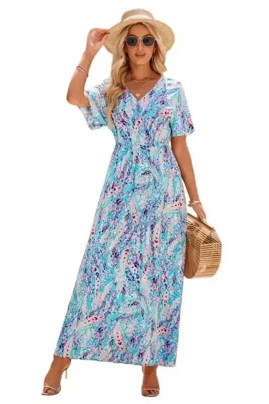 Model in green floral wrap maxi dress with v-neck, accessorized with straw hat and bag, perfect for beach or resort wear.