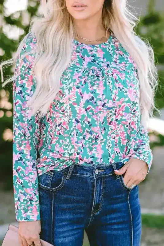 Close-up of green floral long sleeve top with abstract pink and purple print, tucked into high-waisted jeans.