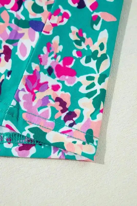 Close-up of sleeve hem on green floral print top, highlighting stitching and colorful abstract pattern.
