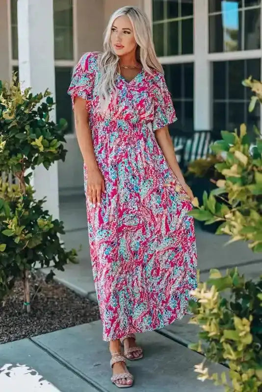 Woman posing in pink floral maxi dress with v-neck and wrap design, perfect for garden parties or summer gatherings.