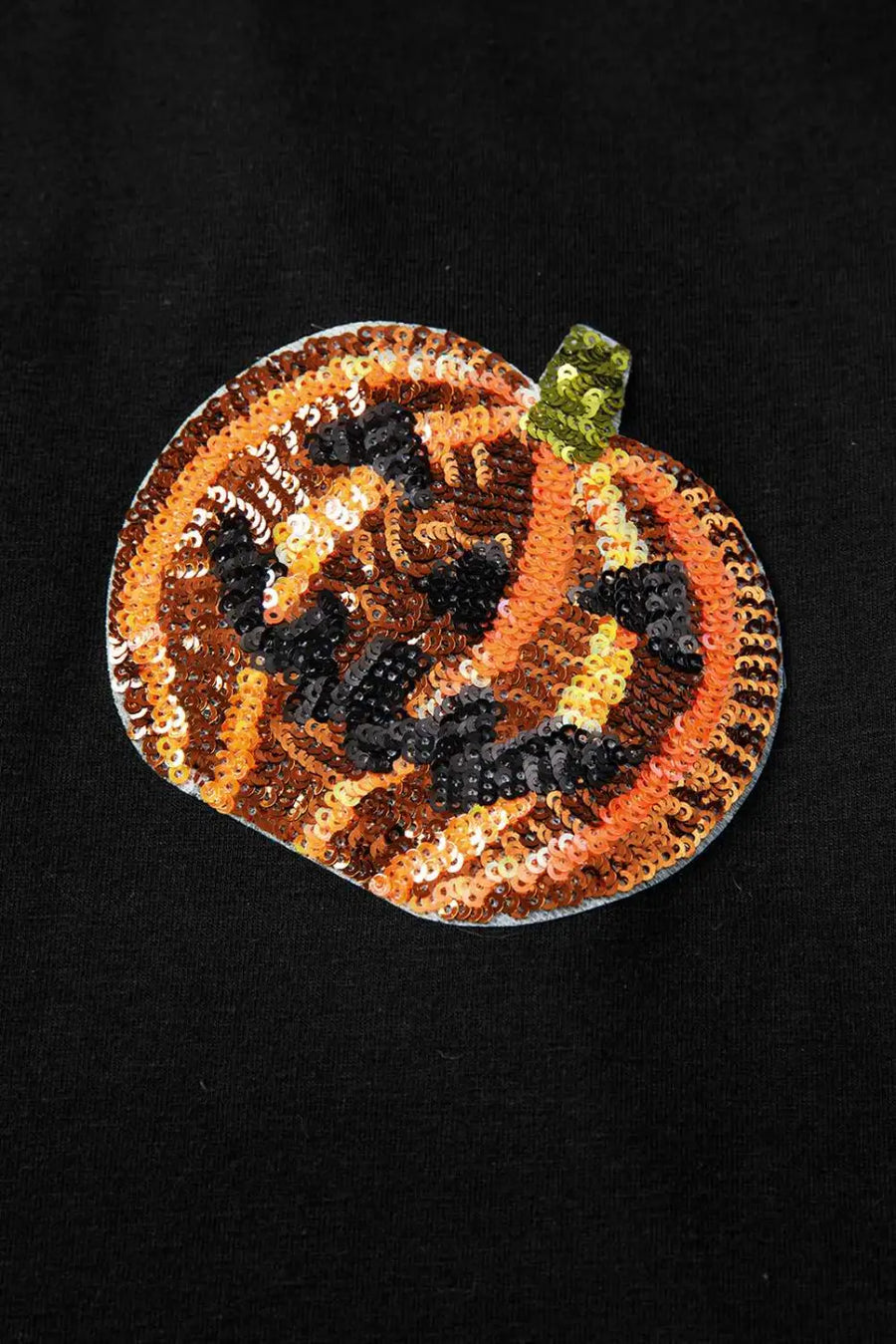 Black shirt with sequin pumpkin designs on a beige background