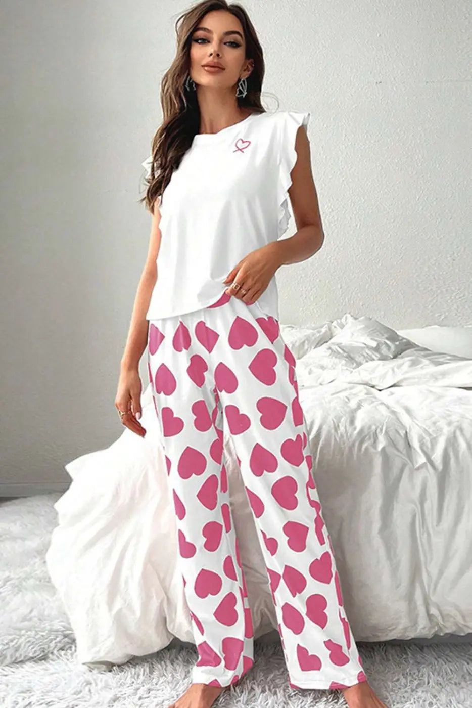 Woman wearing a white top and pink heart-patterned pants in a bedroom setting.