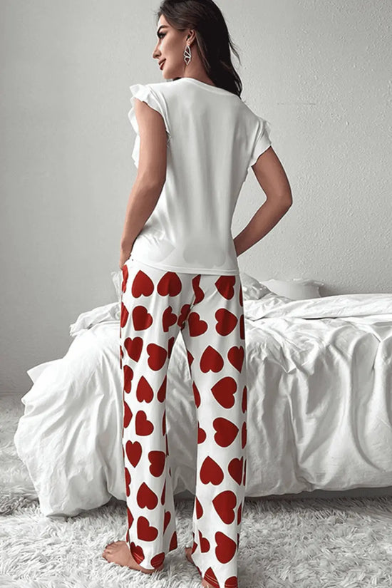 Woman wearing a white top and red heart-patterned pants in a bedroom setting.