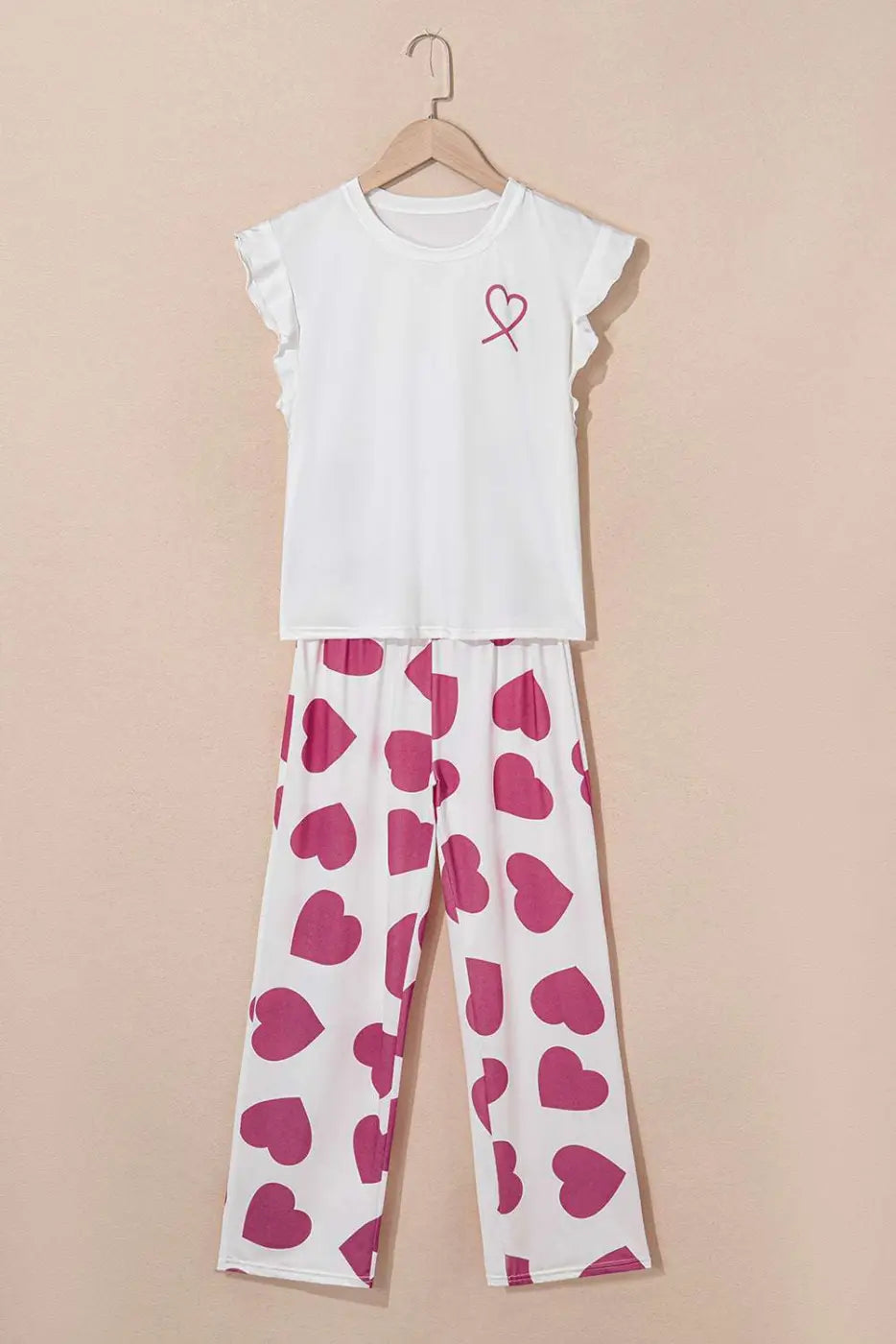 White top with a pink heart design and heart-patterned pants on a beige background