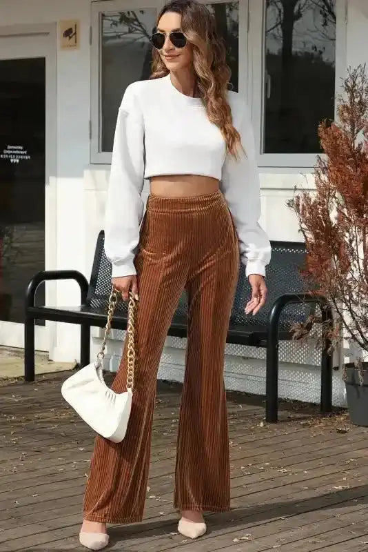 Chic women's flare corduroy pants in brown with high waist and wide leg silhouette, styled with a white crop top for a modern casual look.