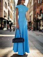 Woman in a blue dress holding a black handbag on a sidewalk.