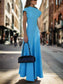 Woman in a blue dress holding a black handbag on a sidewalk.
