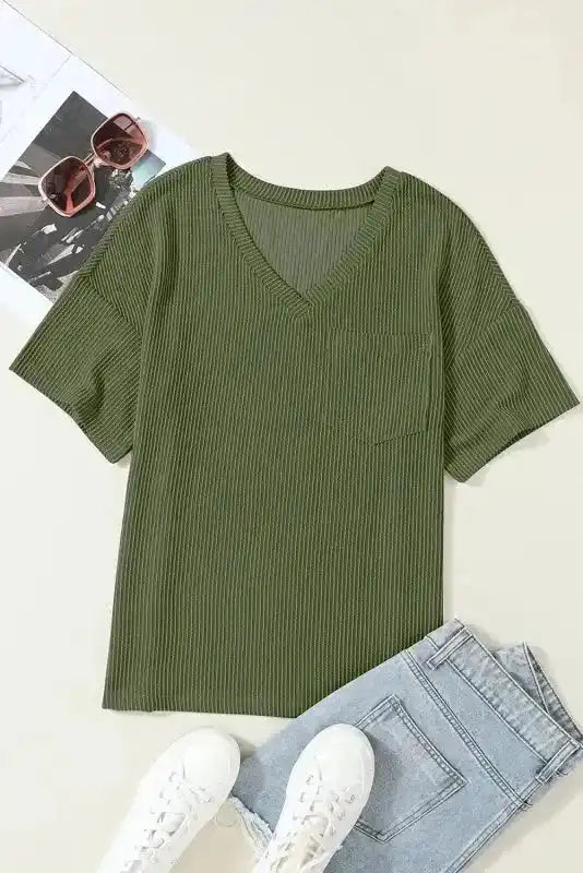 Flat lay of olive green corded V-neck loose T-shirt with chest pocket, paired with denim and sneakers for a casual outfit idea.