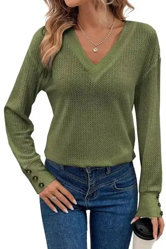 Women's jungle green V-neck jumper with textured knit and buttoned cuffs, styled casually with jeans and a coffee cup.