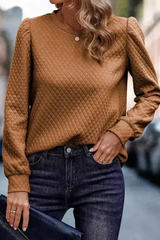 Front view of camel brown quilted hooded dress with kangaroo pocket and puff sleeves, styled with dark denim jeans for a casual look.