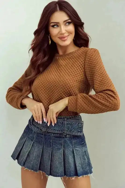 Model smiling in camel quilted hooded dress and pleated denim mini skirt, combining comfort and fashion for casual occasions.