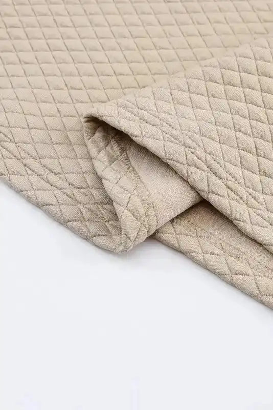 Folded hem of quilted hooded dress, highlighting soft beige fabric and diamond quilted texture for cozy wear.
