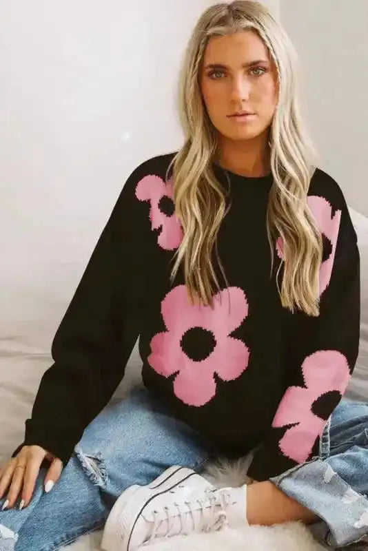 Model wearing khaki floral drop shoulder sweater with bold pink floral print, styled for a relaxed everyday outfit with distressed jeans.