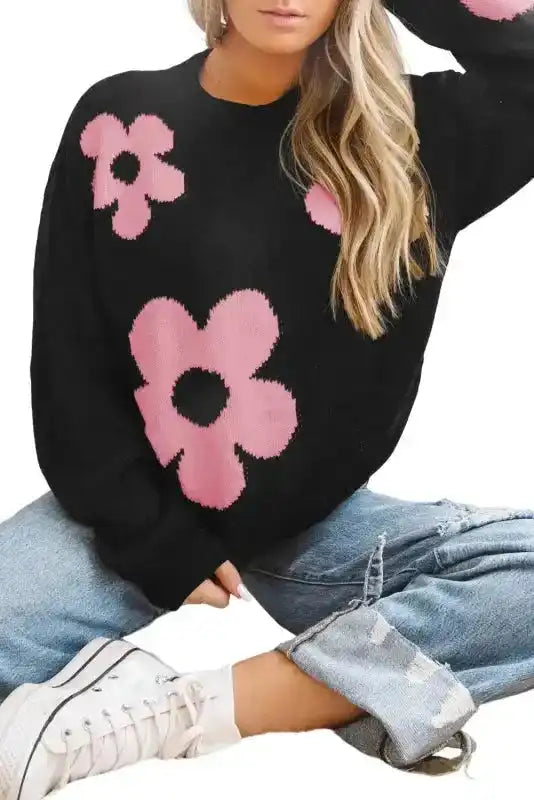 Khaki floral drop shoulder sweater in black with pink flower design, shown in a seated pose highlighting its relaxed fit and cozy texture.