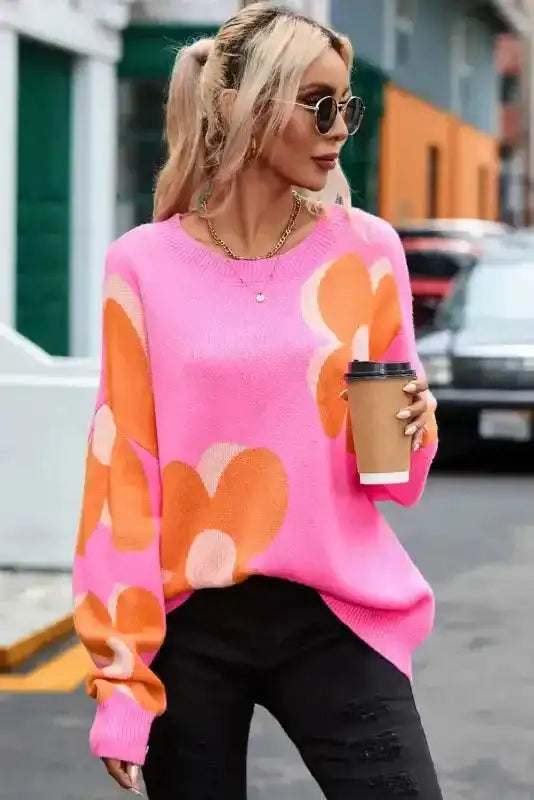 Khaki Floral Drop Shoulder Sweater in bright pink with oversized orange floral print, styled with black jeans and coffee cup for casual streetwear.