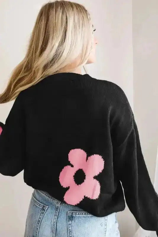 Back view of khaki floral drop shoulder sweater featuring a large pink flower print near the hem, paired with light-wash denim jeans.