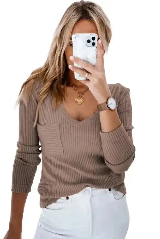Khaki ribbed V-neck knit top with chest pocket, styled for a casual look with white jeans and gold accessories.
