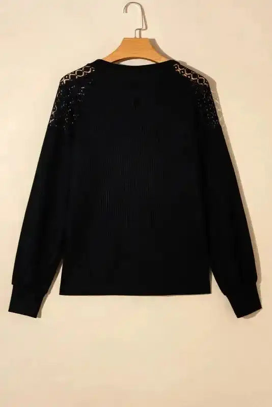 Back of Black Lace Sleeve Textured Top displayed on hanger, highlighting lace details and ribbed knit fabric.
