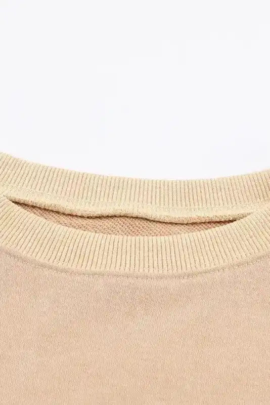 Close-up of ribbed neckline on beige sweatshirt, highlighting soft fabric texture and quality stitching for comfort and durability.