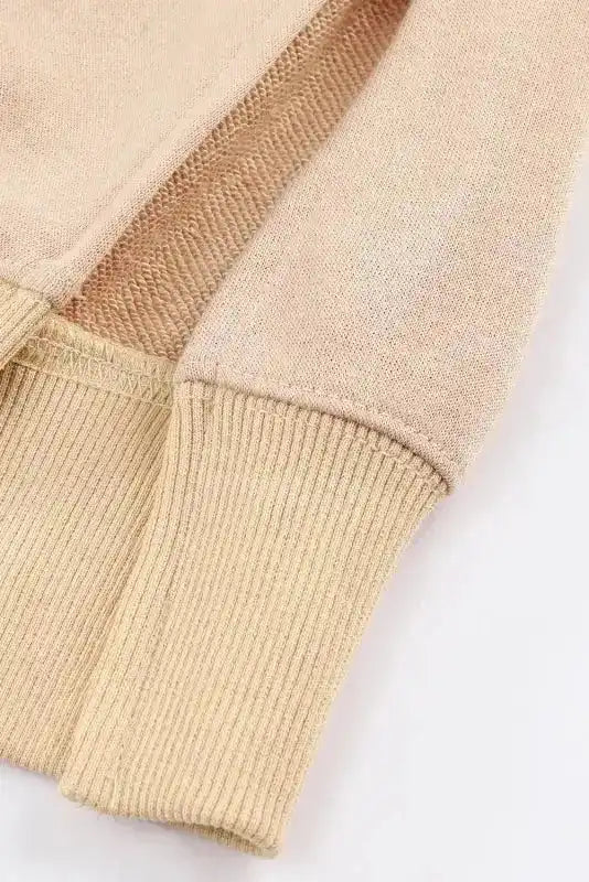 Close-up of sleeve and hem stitching on beige sweatshirt, emphasizing craftsmanship and soft, warm fabric ideal for winter wear.