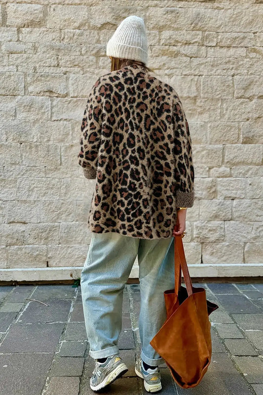 Person wearing a leopard print coat and light blue jeans, standing against a stone wall.