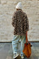 Person wearing a leopard print coat and light blue jeans, standing against a stone wall.
