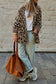 Person wearing a leopard print coat, light blue jeans, and holding a brown bag against a stone wall.