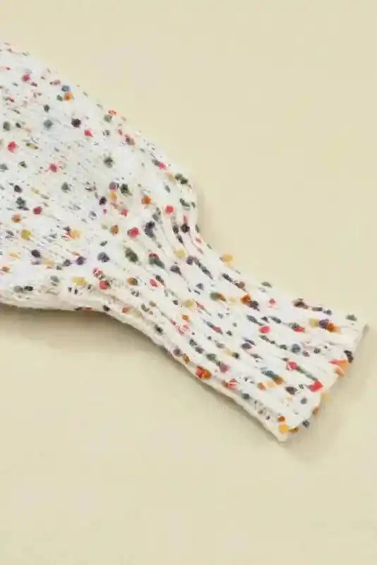 Detail of ribbed cuff on white colorful cable knit sweater with vibrant dots. Adds texture and warmth to your winter wardrobe.