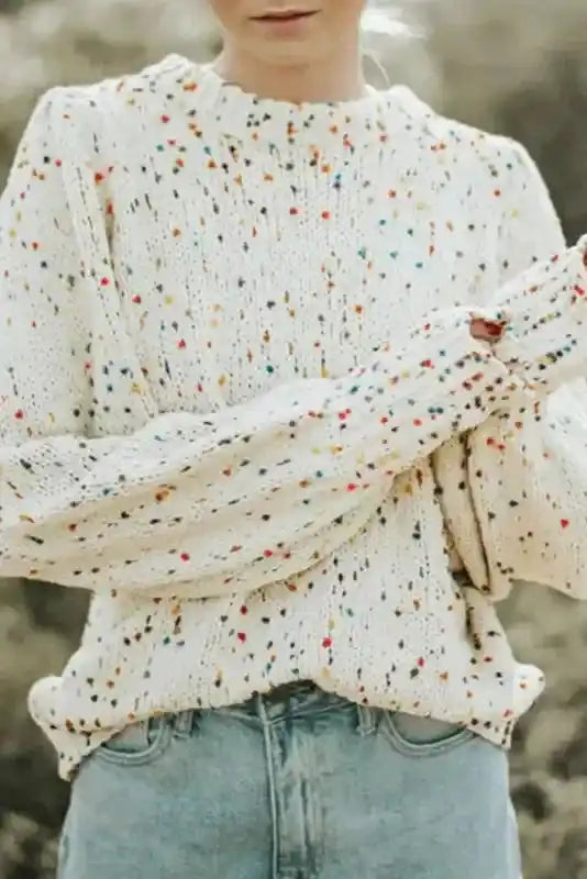 Colorful cable knit sweater in white with multicolor dots, styled with puff sleeves and ribbed hem. Cozy winter top for casual layering.