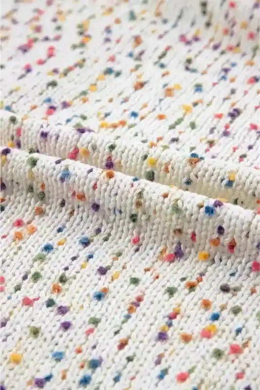 Fabric close-up of colorful cable knit sweater, featuring soft white knit with vibrant multicolor dots for cozy winter style.