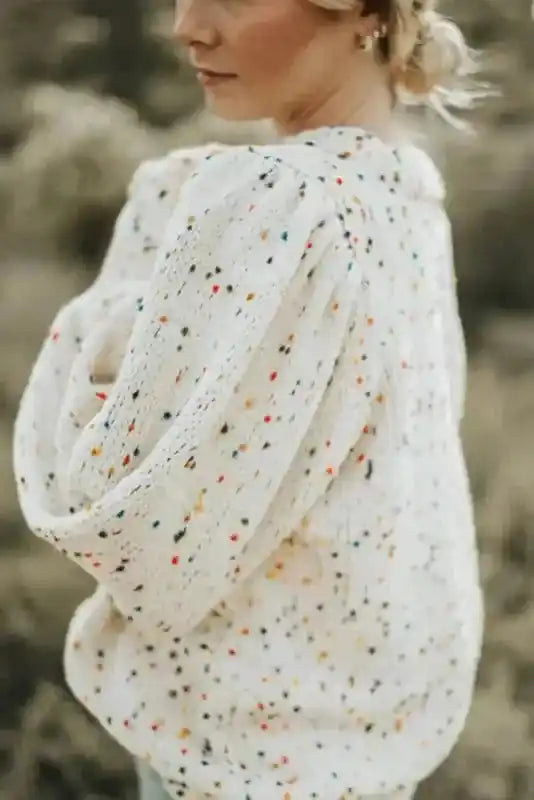 Side view of white cable knit sweater with colorful dots and textured sleeves. A warm and stylish winter top for everyday wear.