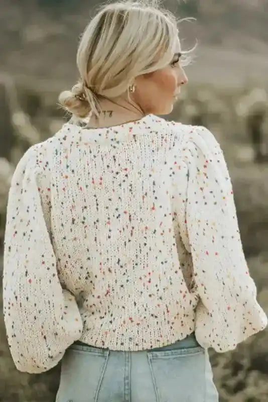 Back view of white colorful cable knit sweater with vibrant speckles and balloon sleeves. Ideal for daily winter fashion.