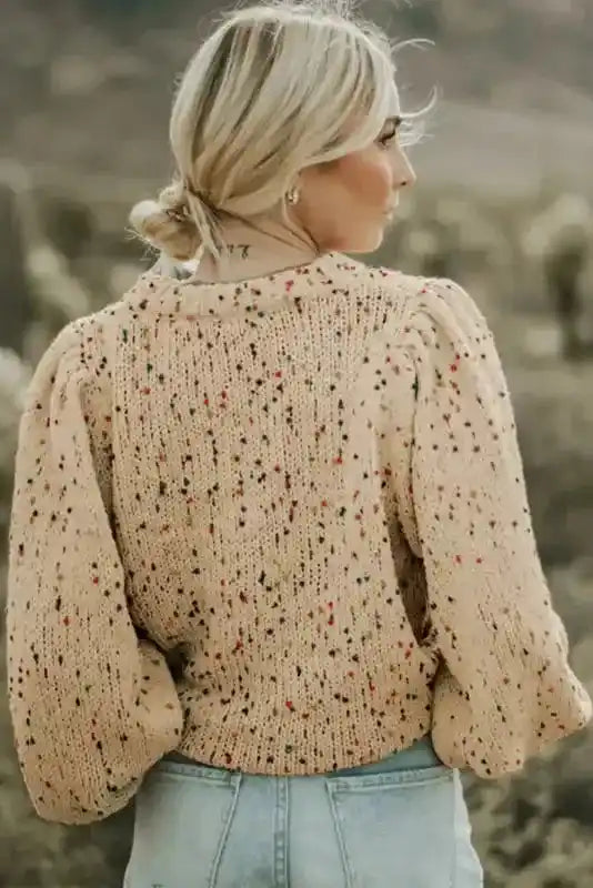 Back view of colorful cable knit sweater in beige, featuring textured knit and vibrant dot accents. Perfect for daily winter outfits.
