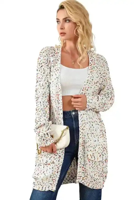 Model wearing colorful cable knit sweater cardigan with multicolor dots, styled open with jeans and a white crop top.