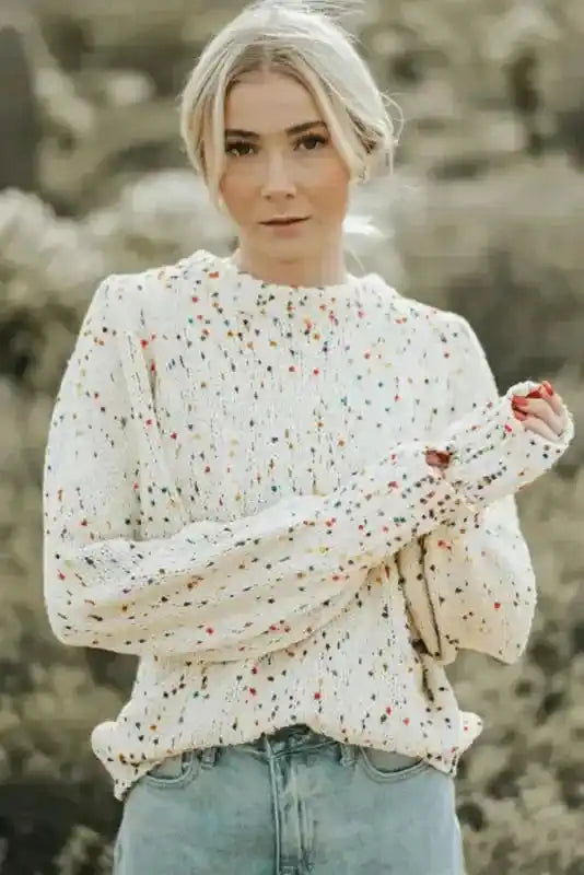 Front view of white colorful cable knit sweater with multicolor speckles and ribbed cuffs. Cozy pullover for winter layering.
