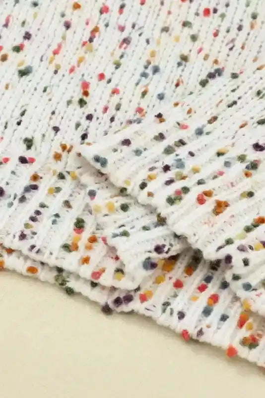 Close-up of hem on white colorful cable knit sweater with multicolor speckles. Cozy and stylish knitwear for cold weather.